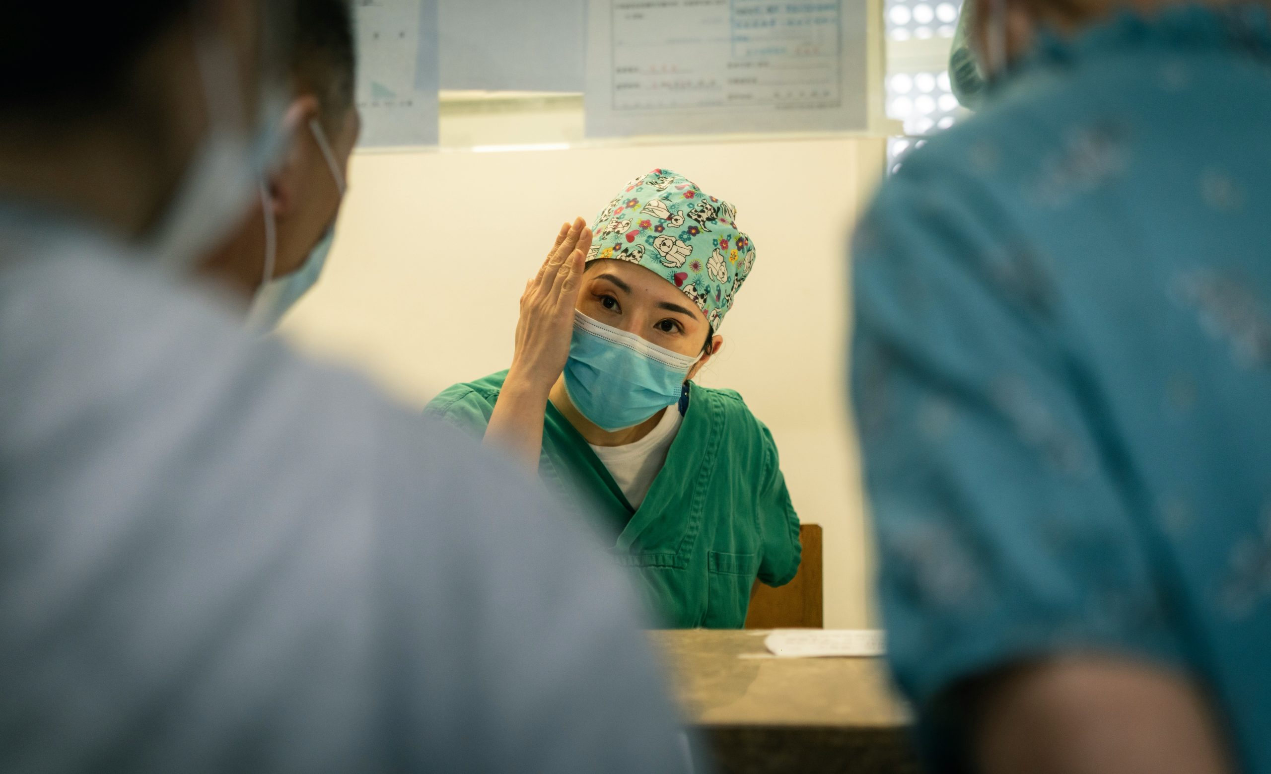 Image shows Paediatrician with a mask, holding the side of their face to demonstrate to two other medical professionals who are back to camera