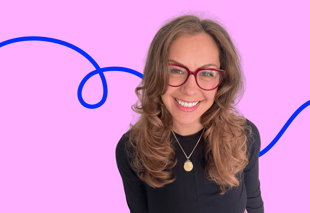 Alenka NHS communication leader with curly hair, red glasses and a black top on a pink background