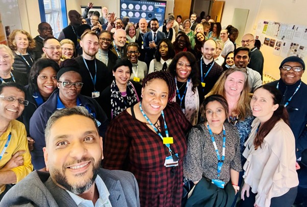 A group of diverse colleagues smiling and posing together for a photo in a modern office setting.